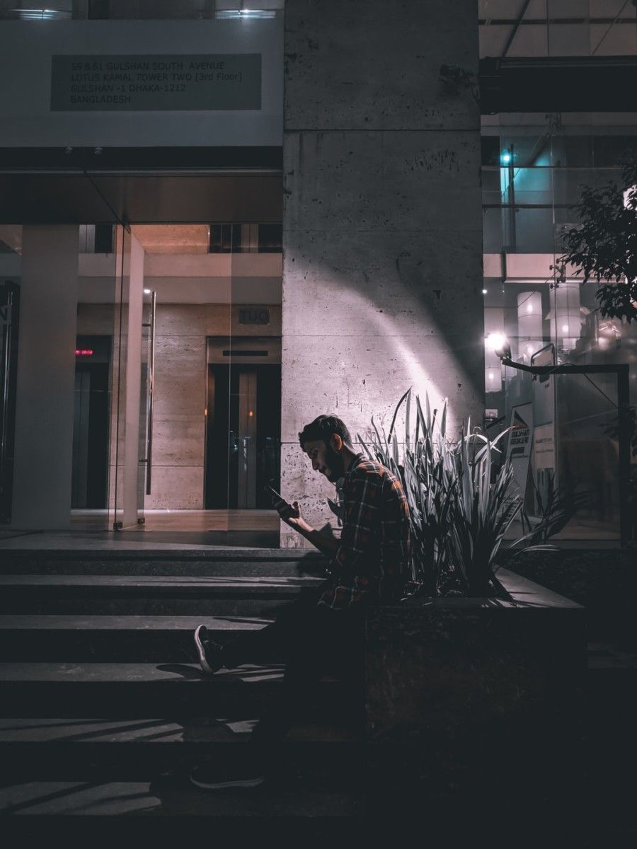 man-sitting-beside-plant-using-smartphone-during-nighttime